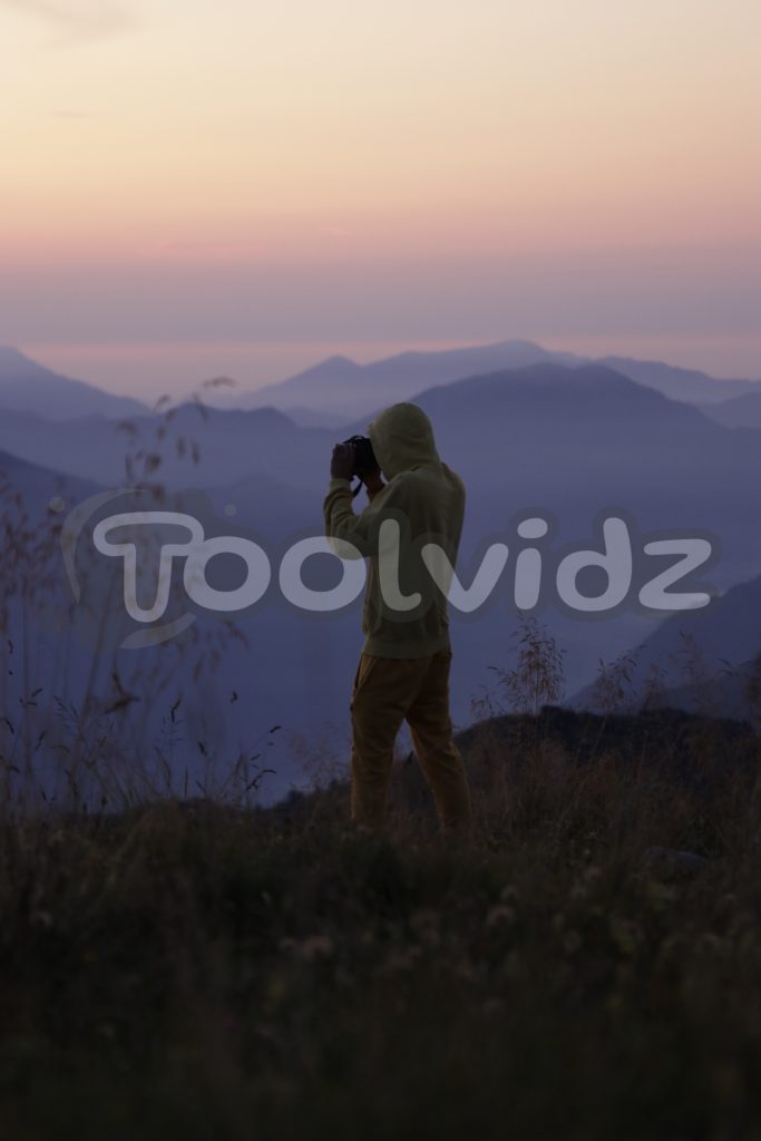 Un giovane fotografo scatta una foto ad un bellissimo panorama montano durante il tramonto. Immagine coperta dal watermark.