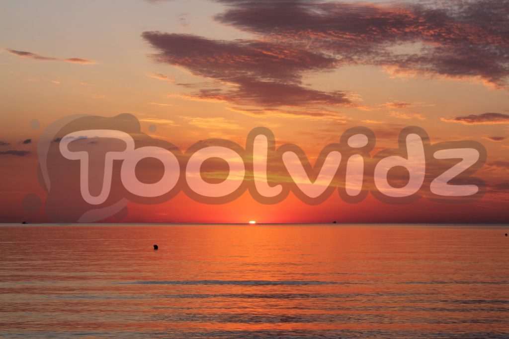 Alba sul mare con un il sole che sta per sorgere al centro dell'inquadratura. Raggi e riflessi arancioni e rossi sul mare e sulle nuvole