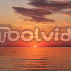 Alba sul mare con un il sole che sta per sorgere al centro dell'inquadratura. Raggi e riflessi arancioni e rossi sul mare e sulle nuvole