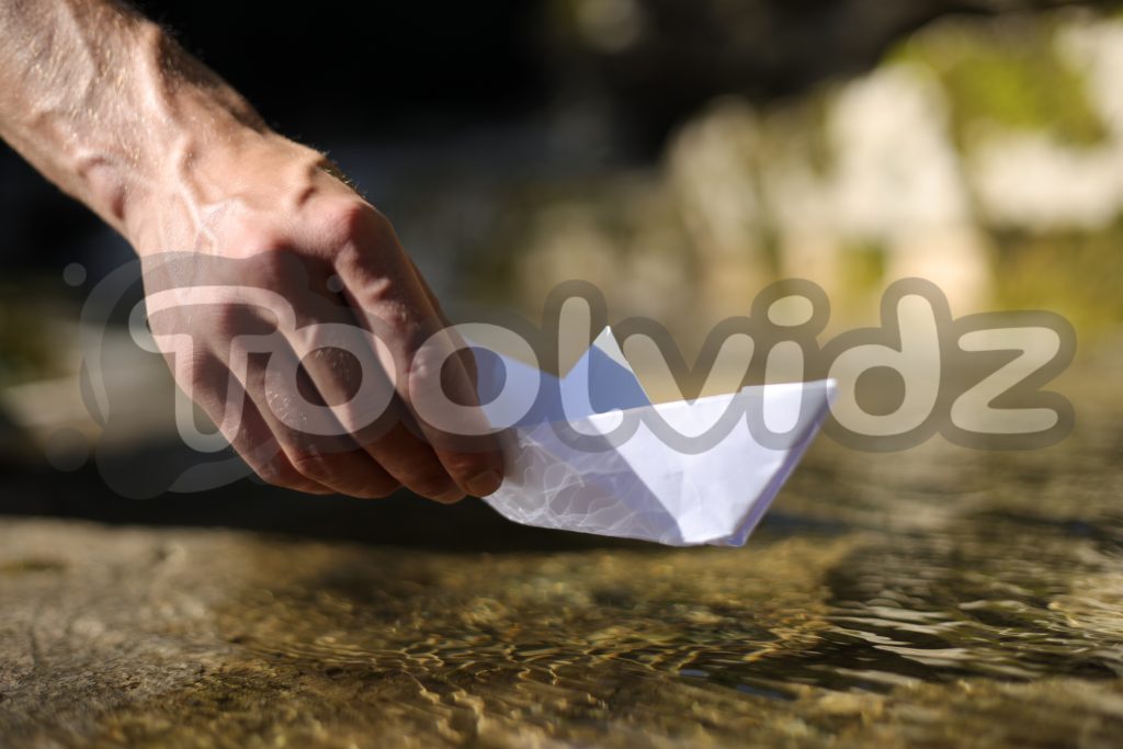 Una mano venosa di un ragazzo giovane appoggia una barca di carta su un telo d'acqua di un ruscello di montagna