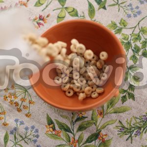 Una tazza vista dall'alto, poggiata su una tovaglia floreale, si sta riempiendo di cereali
