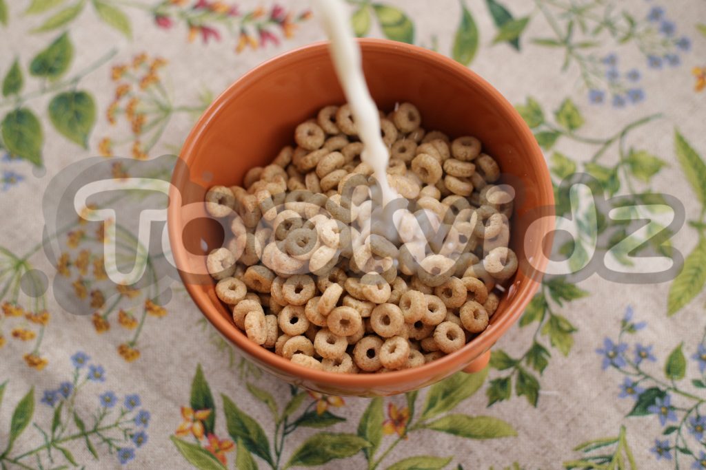 Una tazza arancione piena di cereali posata su una tovaglia floreale si sta riempiendo anche di latte
