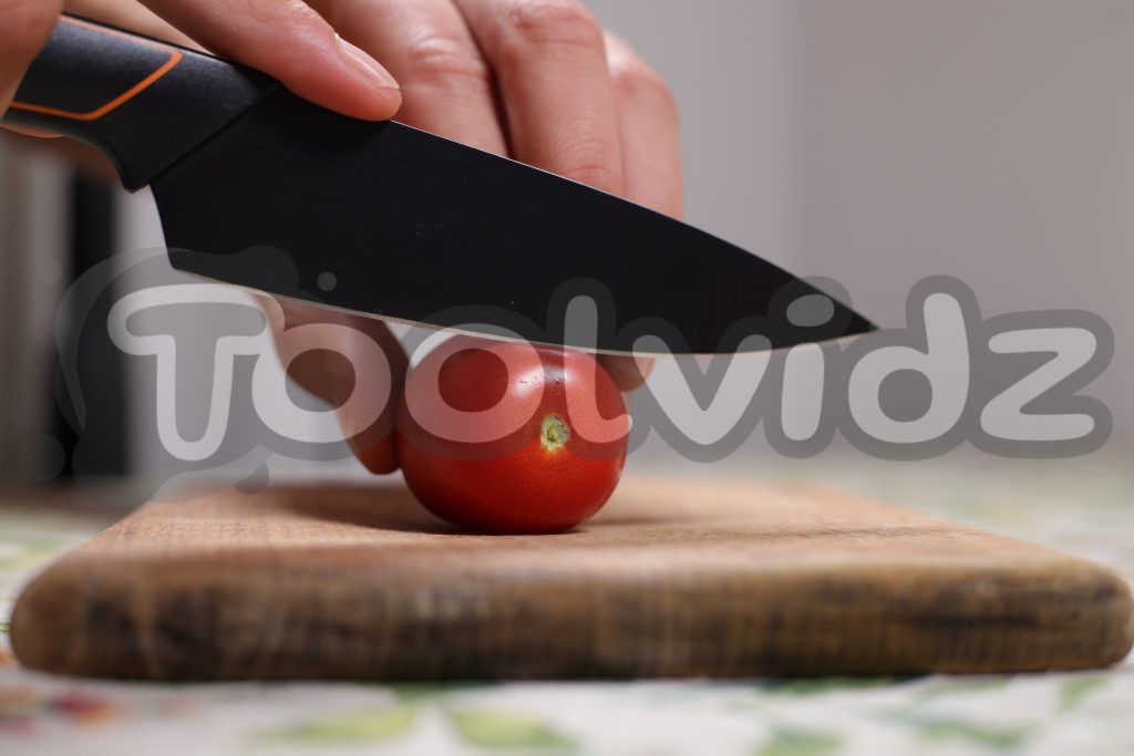 Un pomodoro datterino sta per essere tagliato da un coltello affilato su un tagliere di legno