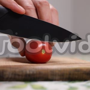 Un pomodoro datterino sta per essere tagliato da un coltello affilato su un tagliere di legno